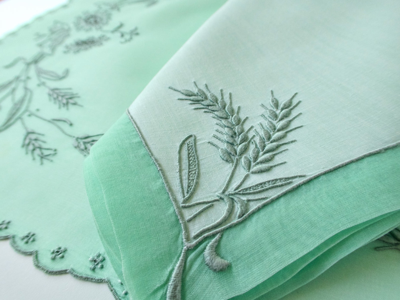 Close-up of a linen napkin embroidered with wheat, folded to show its green underside.