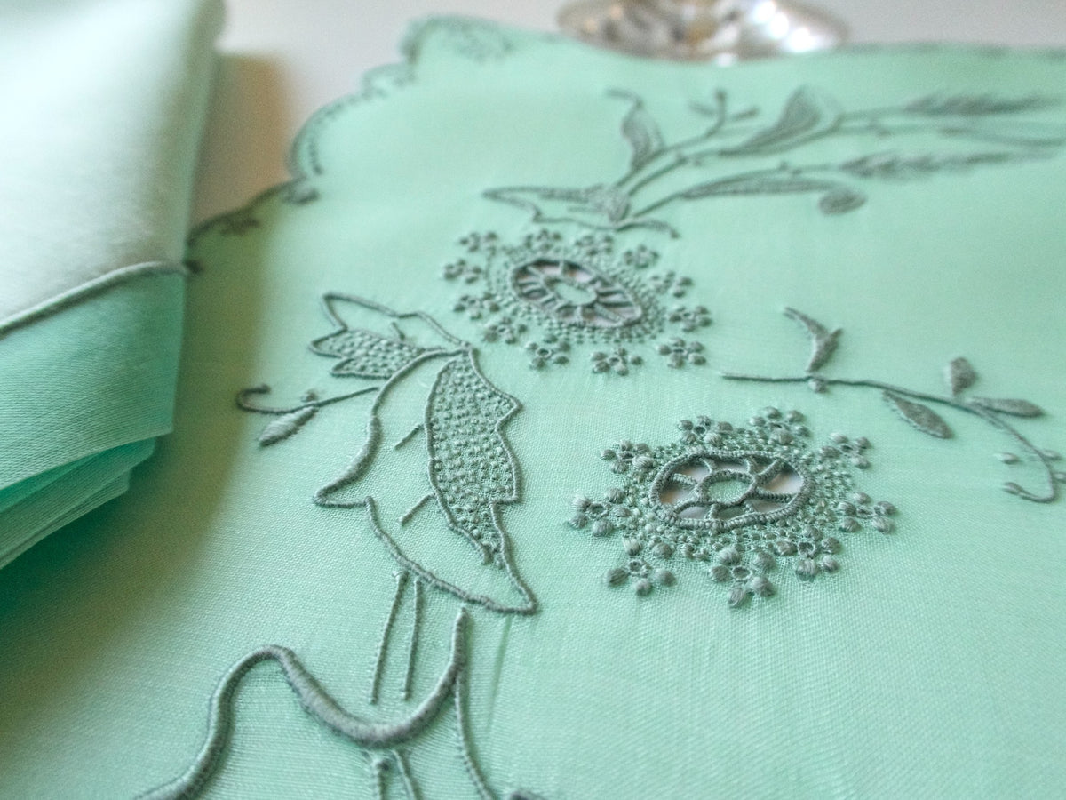 Detail of fine dimensional floral embroidery and small cutwork openings on a green Marghab placemat.