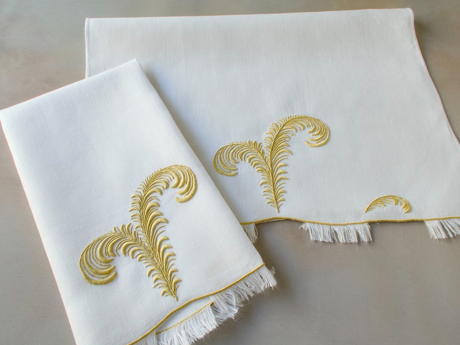 Vintage Marghab linen guest towels in the “Plume” pattern, featuring elegant feather embroidery in gold on fine white linen with eyelash fringe. Hand embroidered in Madeira.