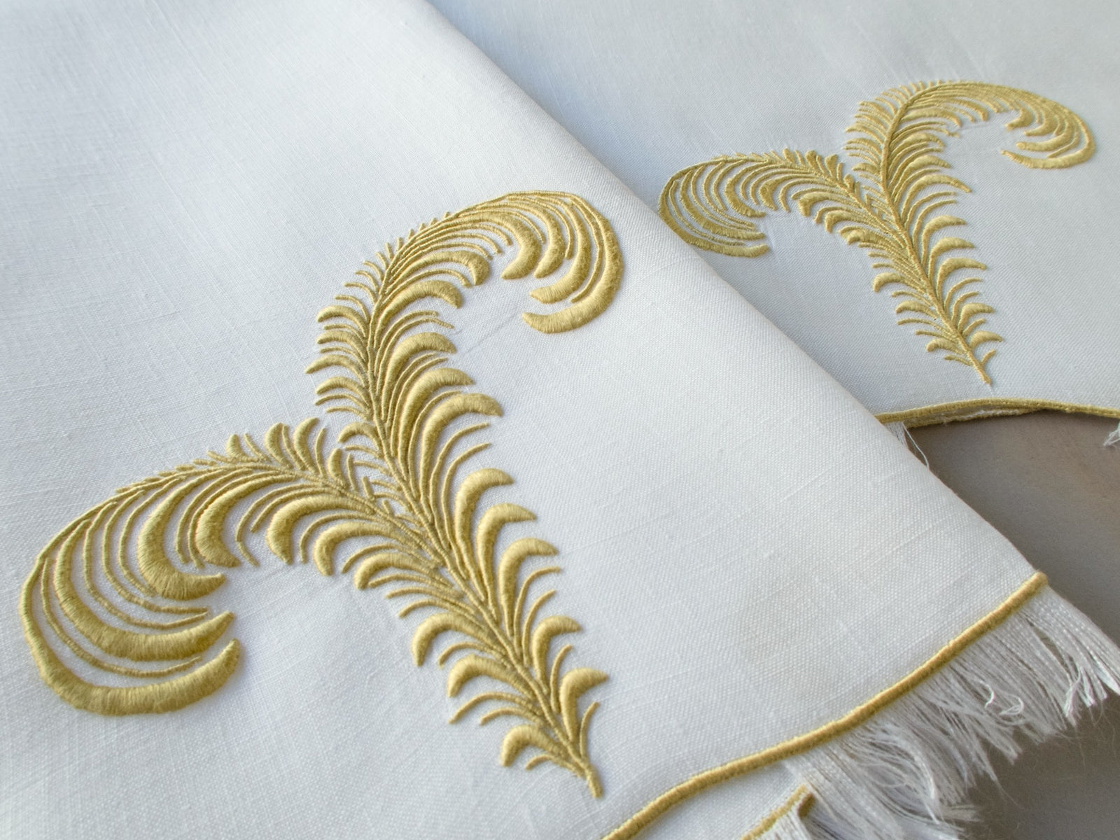 Vintage Marghab linen guest towels in the “Plume” pattern, featuring elegant feather embroidery in gold on fine white linen with eyelash fringe. Hand embroidered in Madeira.