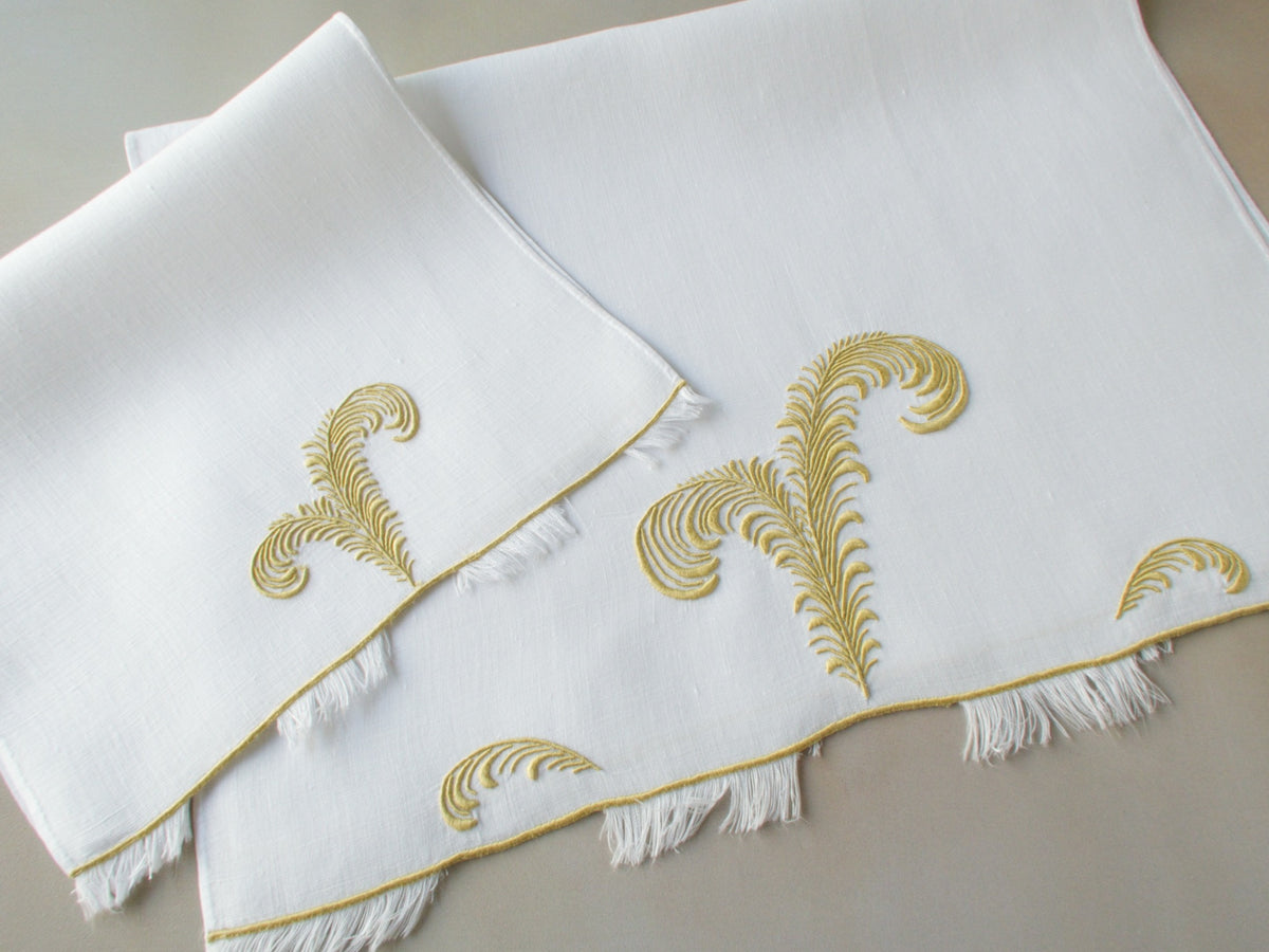 Marghab linen towels in the “Plume” pattern, hand embroidered in gold with feather motifs and eyelash fringe — fingertip and guest sizes shown.
