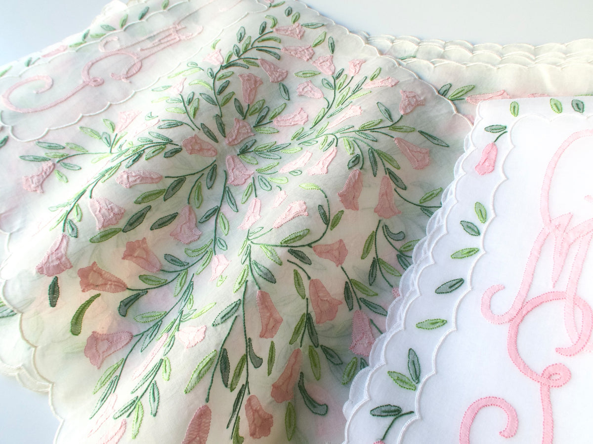 Close-up corner of vintage Madeira organdy placemat with pink shadow work flowers, green stems, and scalloped edge