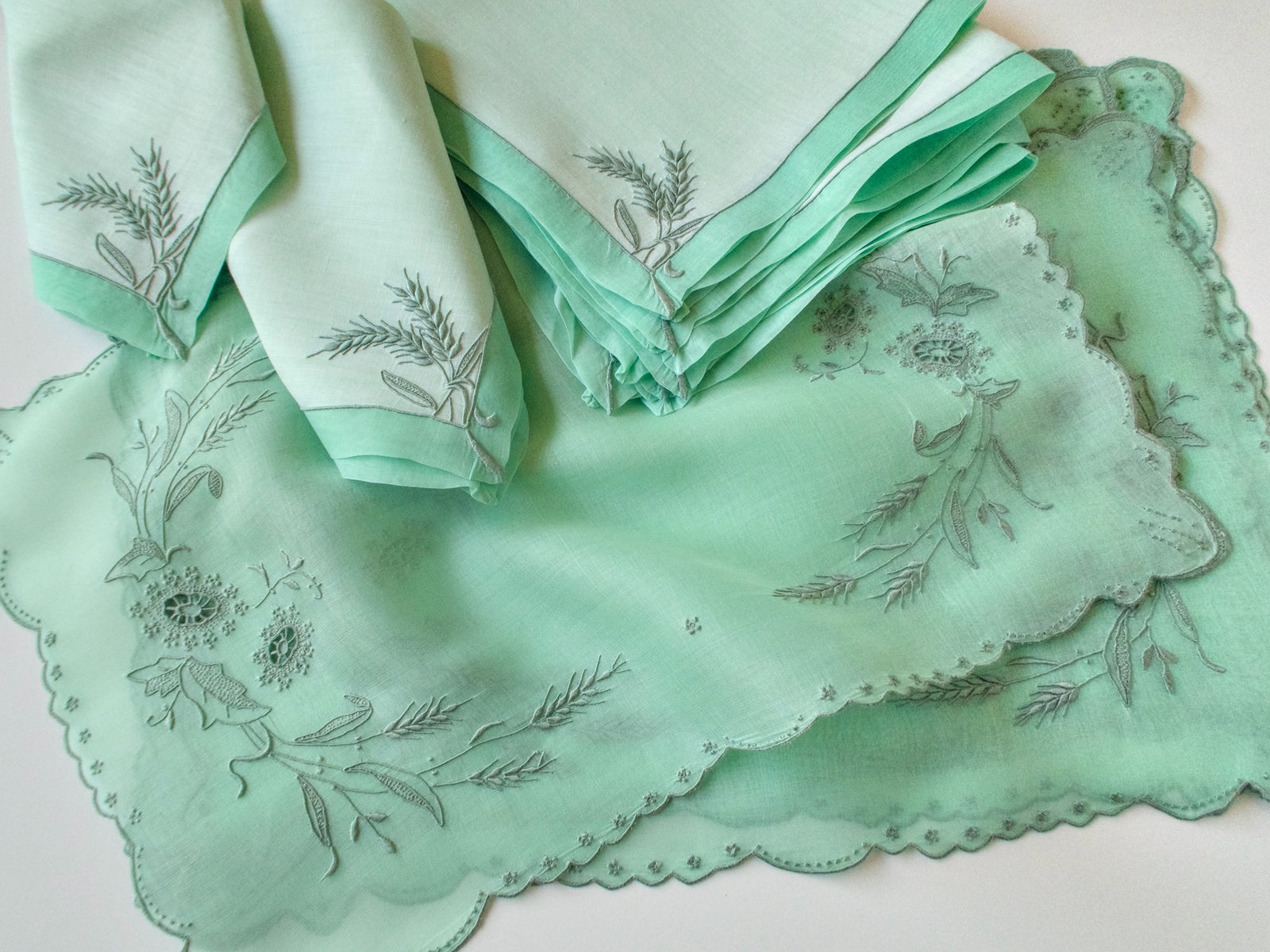 Stack of green Marghab Wheat placemats showing embroidered wheat, floral cutwork and scalloped edges, napkins alongside.