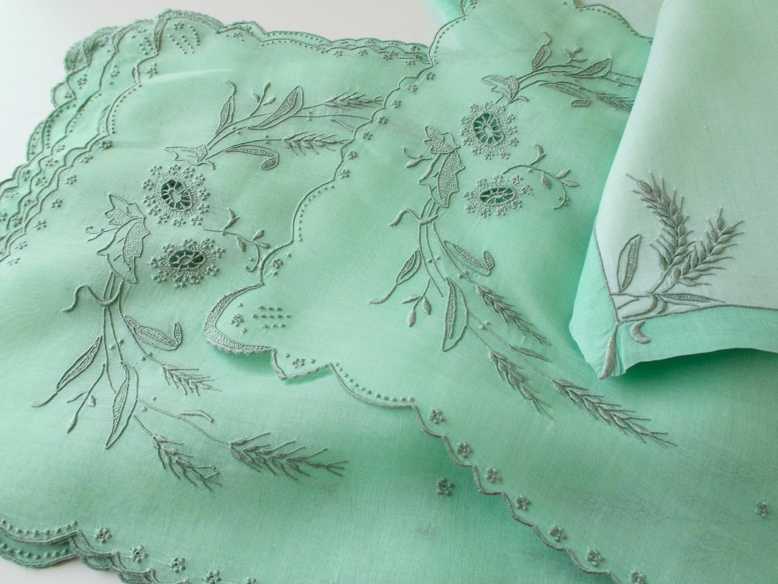 Close-up of green Marghab Wheat placemats with scalloped edges, floral cutwork and a folded embroidered napkin.
