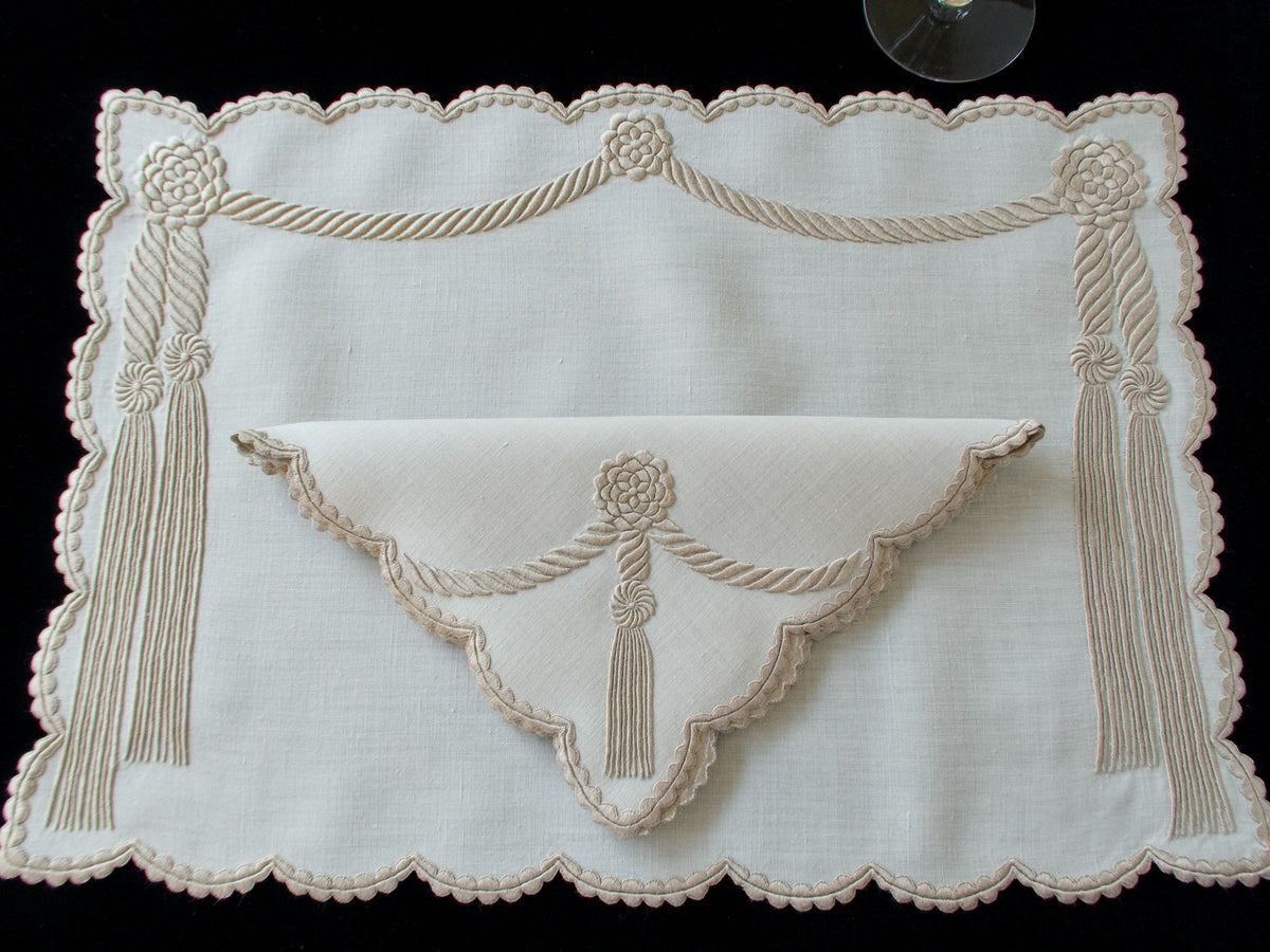 Overhead view of vintage Marghab “Cord &amp; Tassel” placemat and napkin set, hand embroidered in Madeira on fine linen with intricate raised cord and tassel motifs in dimensional relief.