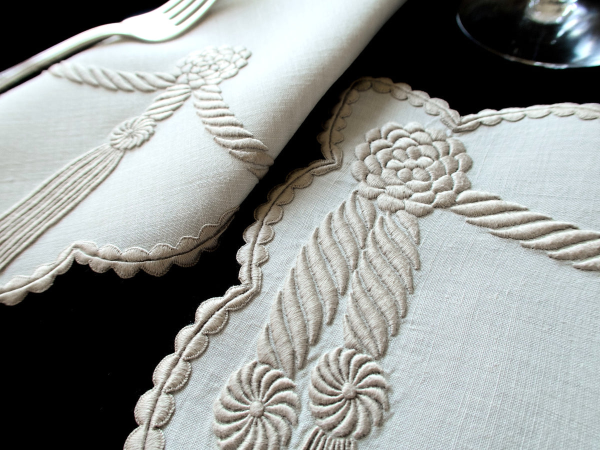 Detail view of vintage Marghab “Cord &amp; Tassel” placemat and napkin set, hand embroidered in Madeira on fine linen with intricate raised cord and tassel motifs in dimensional relief.
