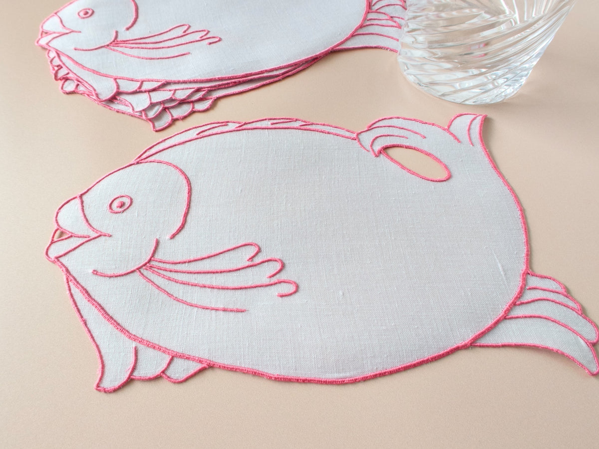 Set of six fish-shaped Madeira linen cocktail napkins outlined in fuchsia embroidery, with crystal glass for scale​​​​​​​​​​​​​​​​