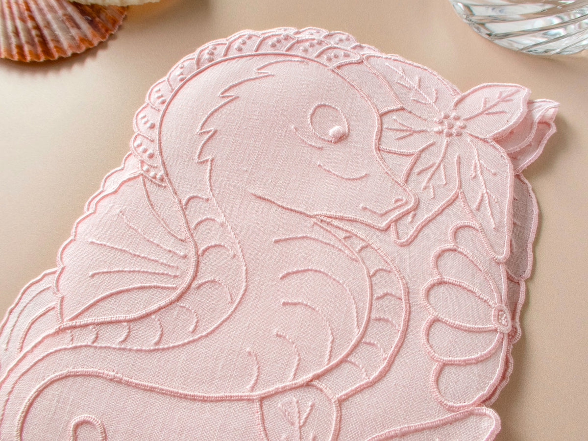 Close-up of vintage Madeira seahorse cocktail napkin showing fine pink linen and detailed hand embroidery​​​​​​​​​​​​​​​​