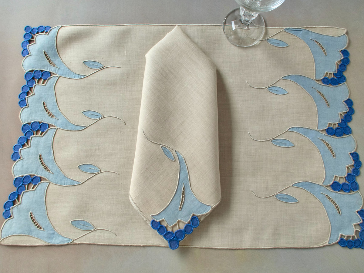 Vintage Marghab “Trumpet Flower” placemat and napkin set with matching table runner, hand embroidered in Madeira in layered blue organdy appliqué with raised trumpet blossom motifs and cutwork detailing.