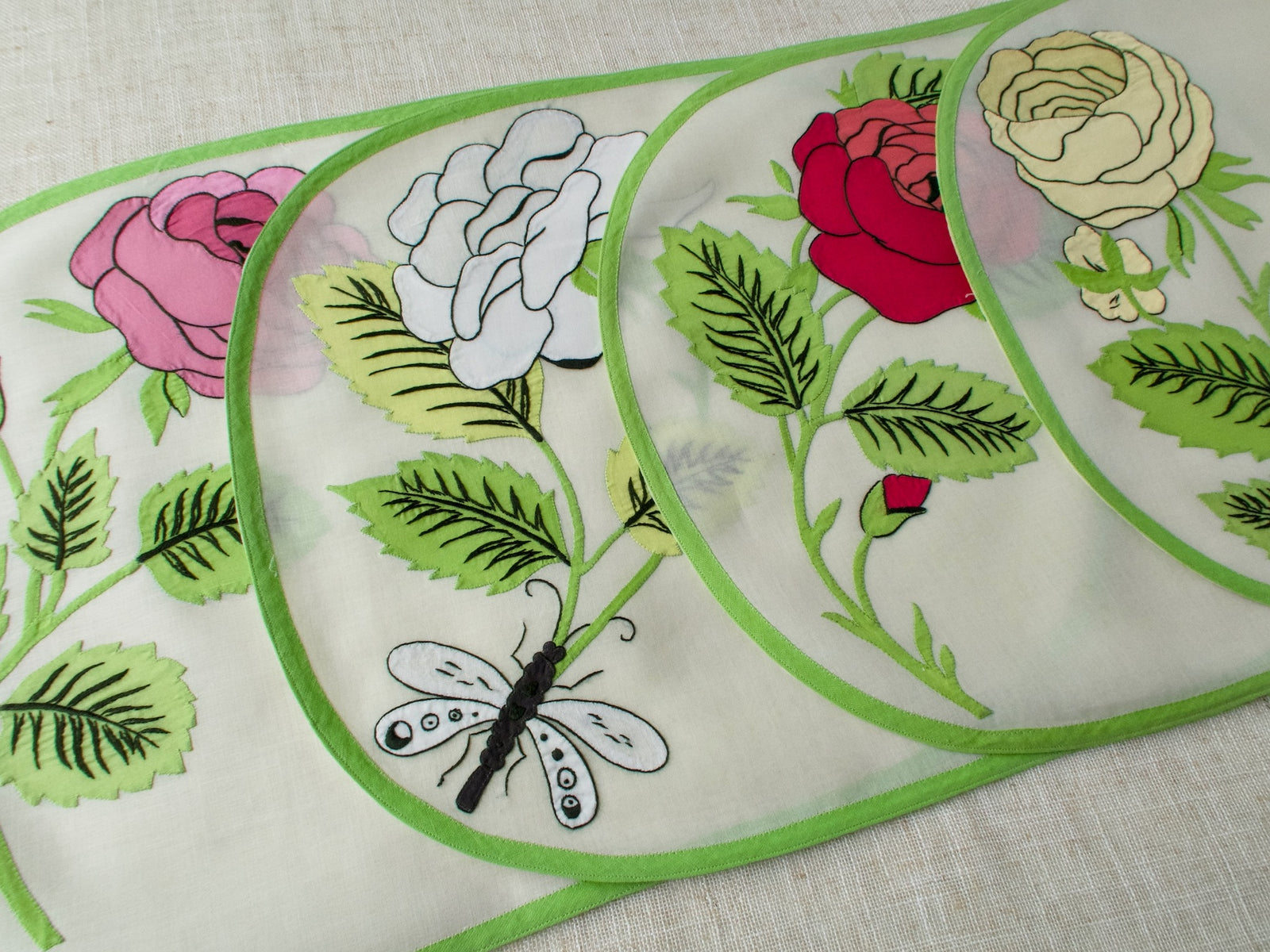 Four vintage Italian appliqué placemats with large-scale roses in red, white, pink, and yellow with dragonfly detail on semi-sheer linen