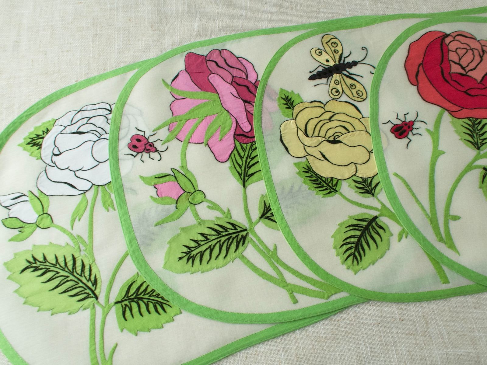 Four vintage Italian appliqué placemats with large-scale roses in red, white, pink, and yellow with ladybug and butterfly detail on semi-sheer linen