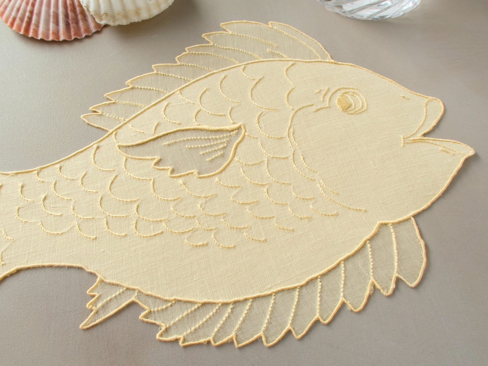 Fish-shaped vintage Irish linen cocktail napkin with hand embroidered scales and organdy fins, hand embroidered in Madeira, on gray background
