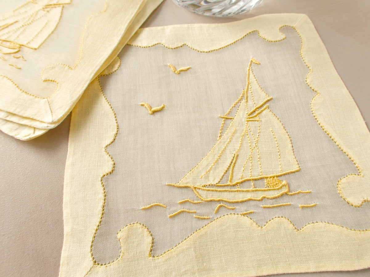 Vintage Madeira linen and organdy cocktail napkin with hand embroidered sailboat, gulls, and ornate repliqué border on beige background