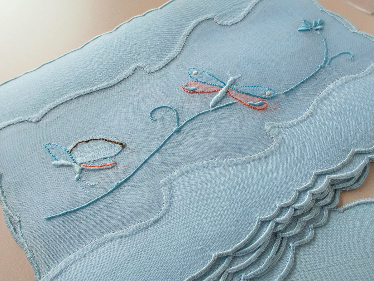 Close-up of vintage Madeira cocktail napkin showing dragonfly in shadow work and satin stitch with orange accents within organdy window