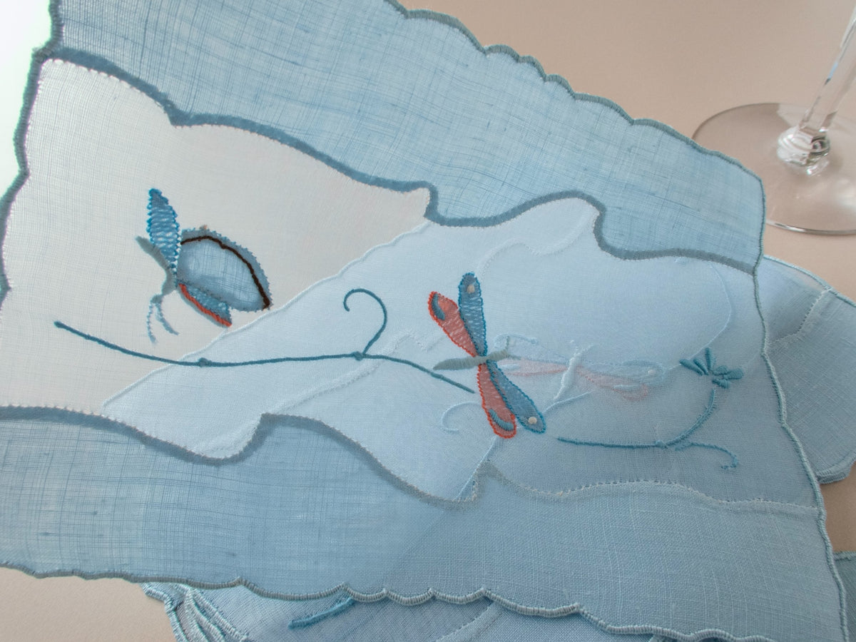 Detail of vintage Madeira cocktail napkin showing butterfly in shadow work and satin stitch with orange accents on organdy and blue linen​​​​​​​​​​​​​​​​