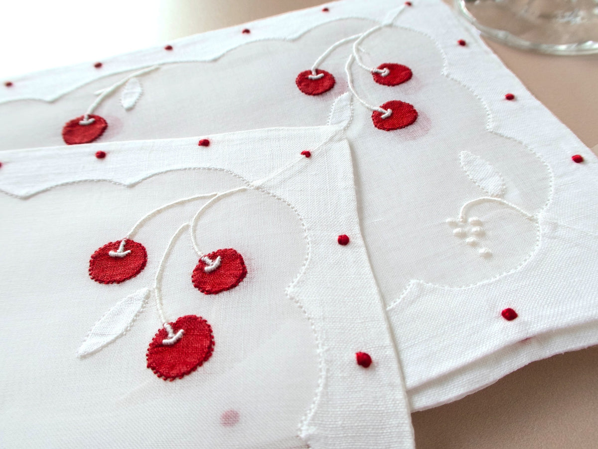 closeup of a vintage Madeira linen and organdy cocktail napkins with red cherry appliqué and white leaf embroidery in organdy center, scalloped repliqué border with red dot accents