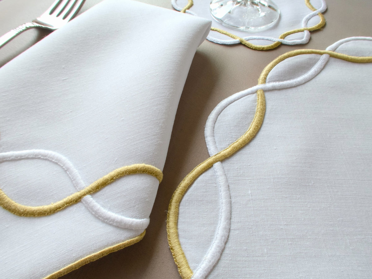 Vintage Marghab “Andante” linen placemat and napkin set, hand embroidered in gold and white on fine linen, featuring the signature looping motif from the rare Andante pattern