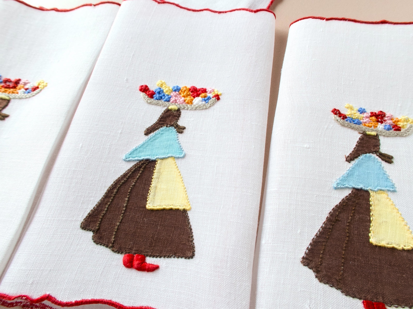 Three vintage Marghab Flower Woman cocktail napkins stacked showing appliqué figure in traditional dress with colorful French knot flower basket