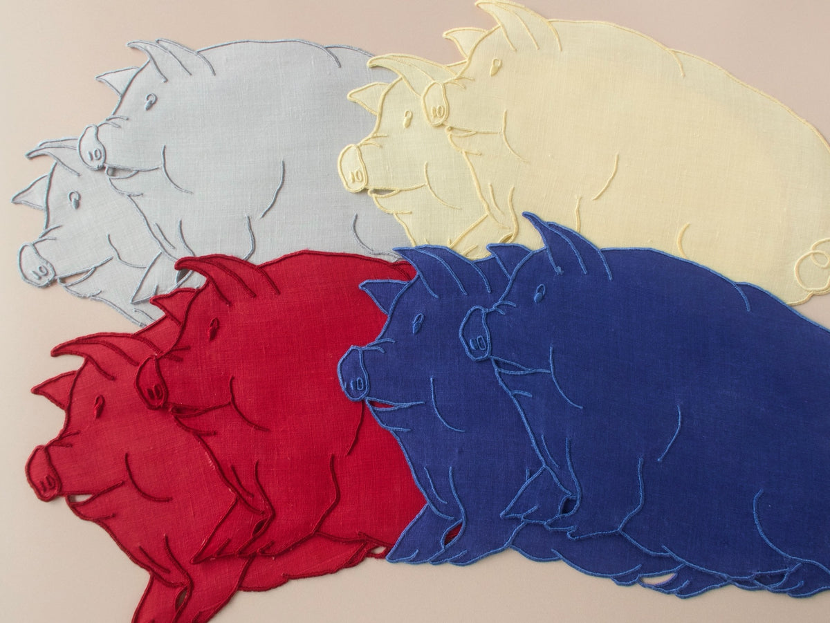 Eight pig-shaped vintage Madeira linen cocktail napkins in red, blue, gray, and yellow fanned out showing expressive faces and curly tails