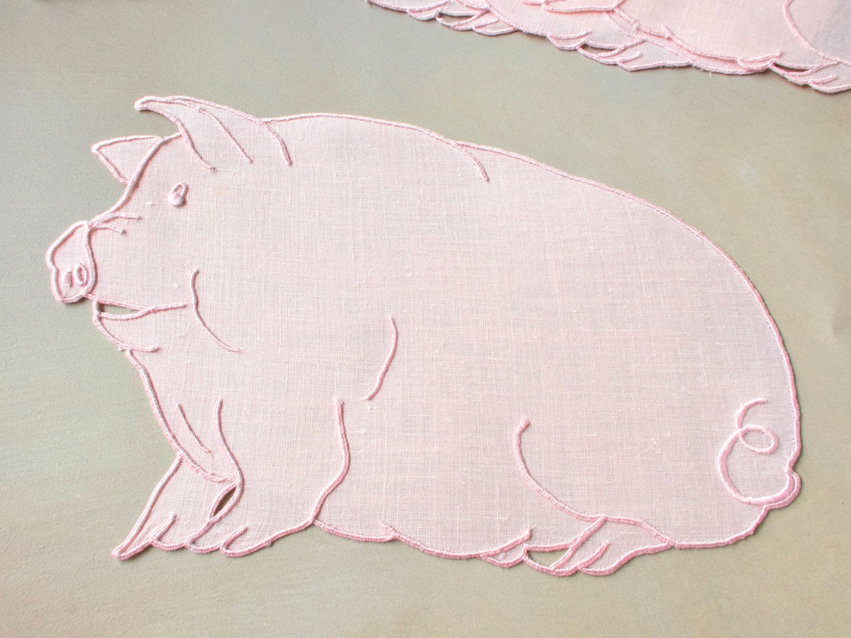 Close-up of a single pink Irish linen cocktail napkin cut and embroidered in the shape of a plump pig with curly tail, Madeira work.​​​​​​​​​​​​​​​​