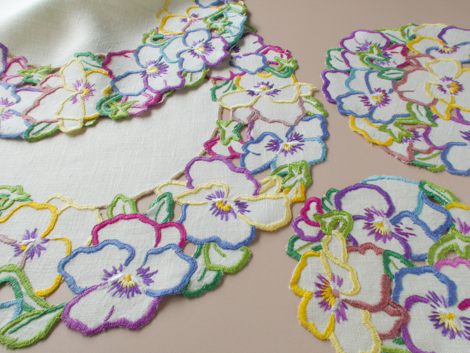 Vintage embroidered pansy coasters and centerpiece on beige background showing full 14-piece placemat set for six.​​​​​​​​​​​​​​​​