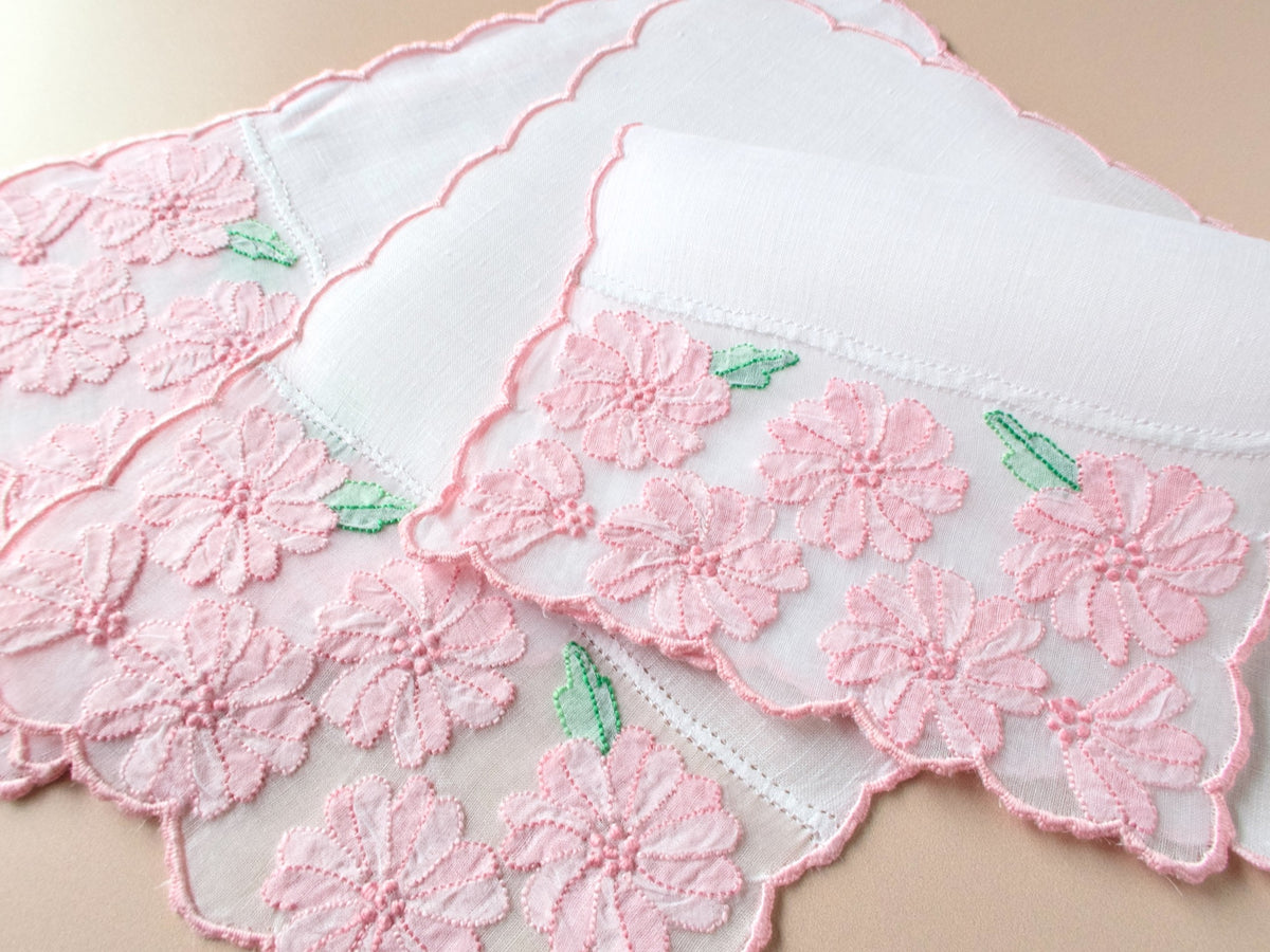 Vintage Madeira cocktail napkins fanned on beige background, pink shadow work flowers embroidered on organdy inset with scalloped pink border.