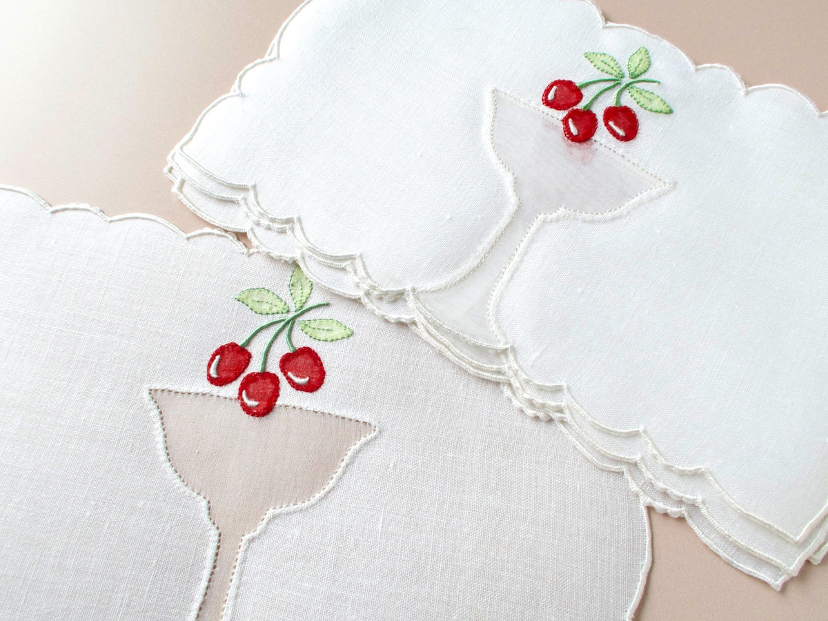 Fanned set of vintage Madeira cherry garnish cocktail napkins on beige background showing organdy goblet inset and red cherry appliqué detail.​​​​​​​​​​​​​​​​
