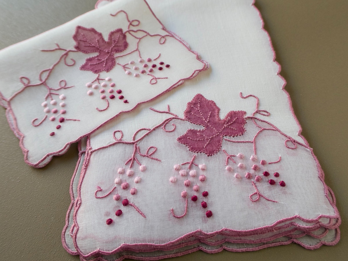 Vintage Madeira cocktail napkins on beige background showing two napkins with organdy window inset and raised pink grape cluster and leaf embroidery with scrolling vines.