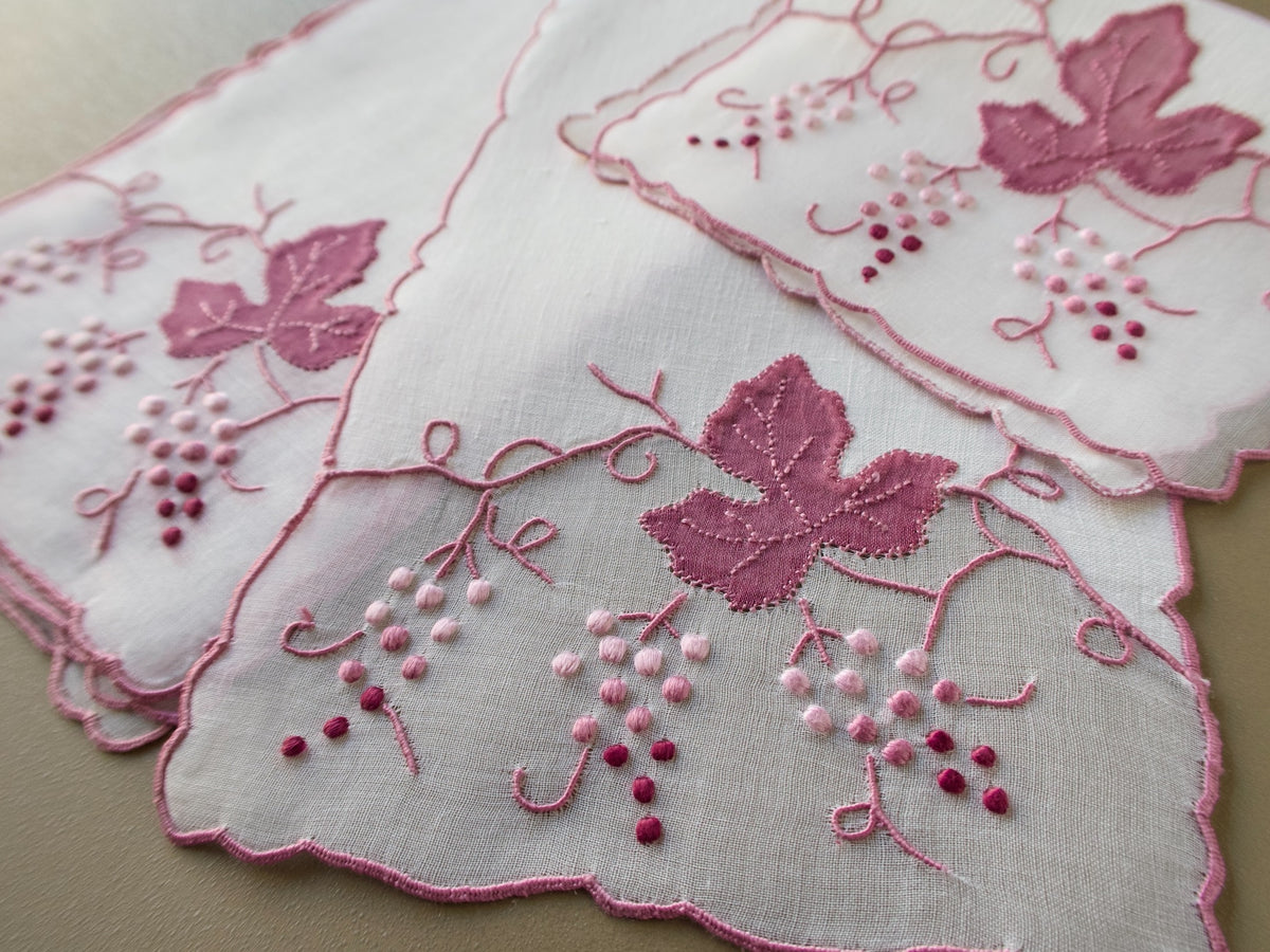 Vintage Madeira cocktail napkins on beige background showing three napkins with organdy window inset and raised pink grape cluster and leaf embroidery with scrolling vines.