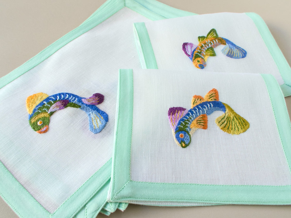 Vintage Léron cocktail napkins fanned and stacked, showing colorful fish embroidery and celadon green border.​​​​​​​​​​​​​​​​