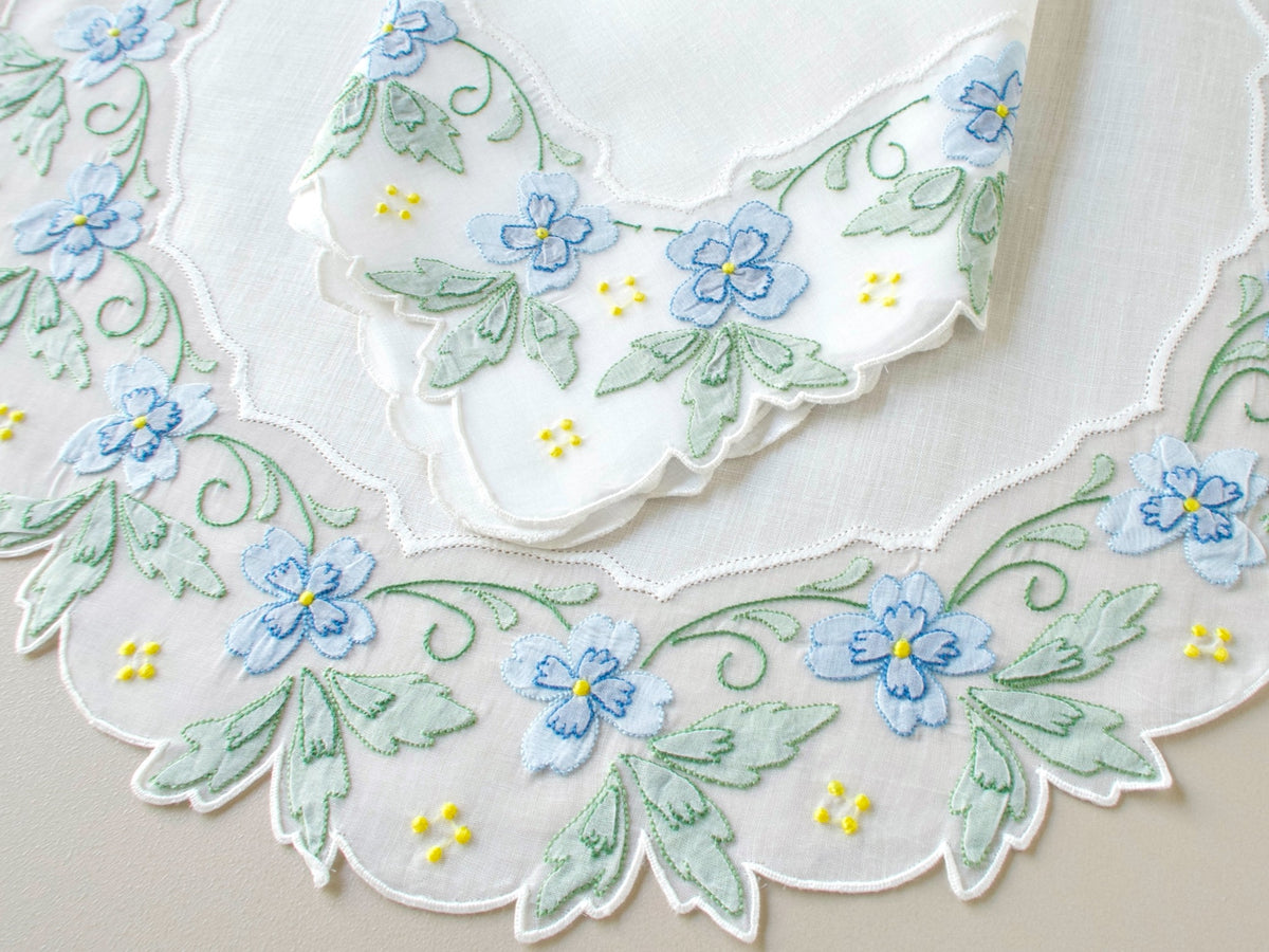 Close-up of hand embroidered blue and green shadow work flowers and leaves with yellow granitos on scalloped organdy border, vintage Madeira placemat