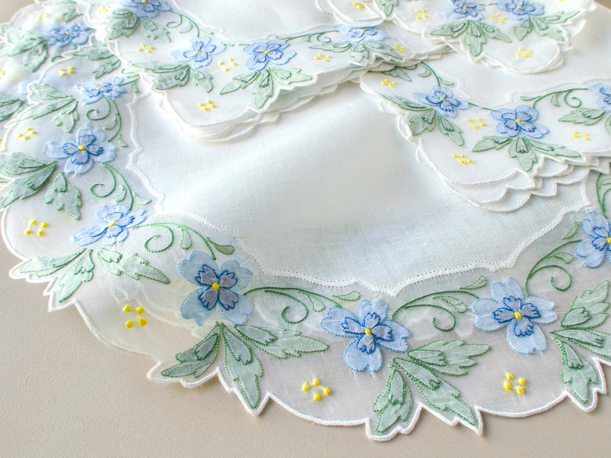 Detail of vintage Madeira placemat and napkin corner showing hand embroidered blue and green shadow work flowers and leaves with yellow granitos on organdy​​​​​​​​​​​​​​​​