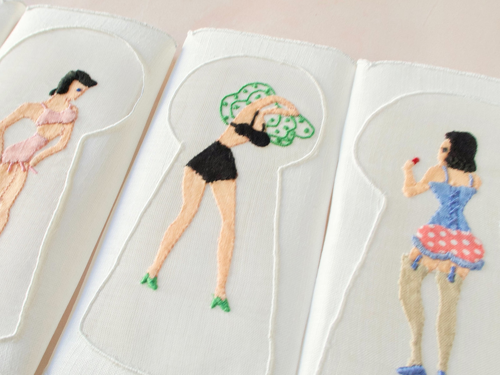 Hand-embroidered Madeira napkin with woman in red polka-dot skirt and black corset viewed through keyhole motif.