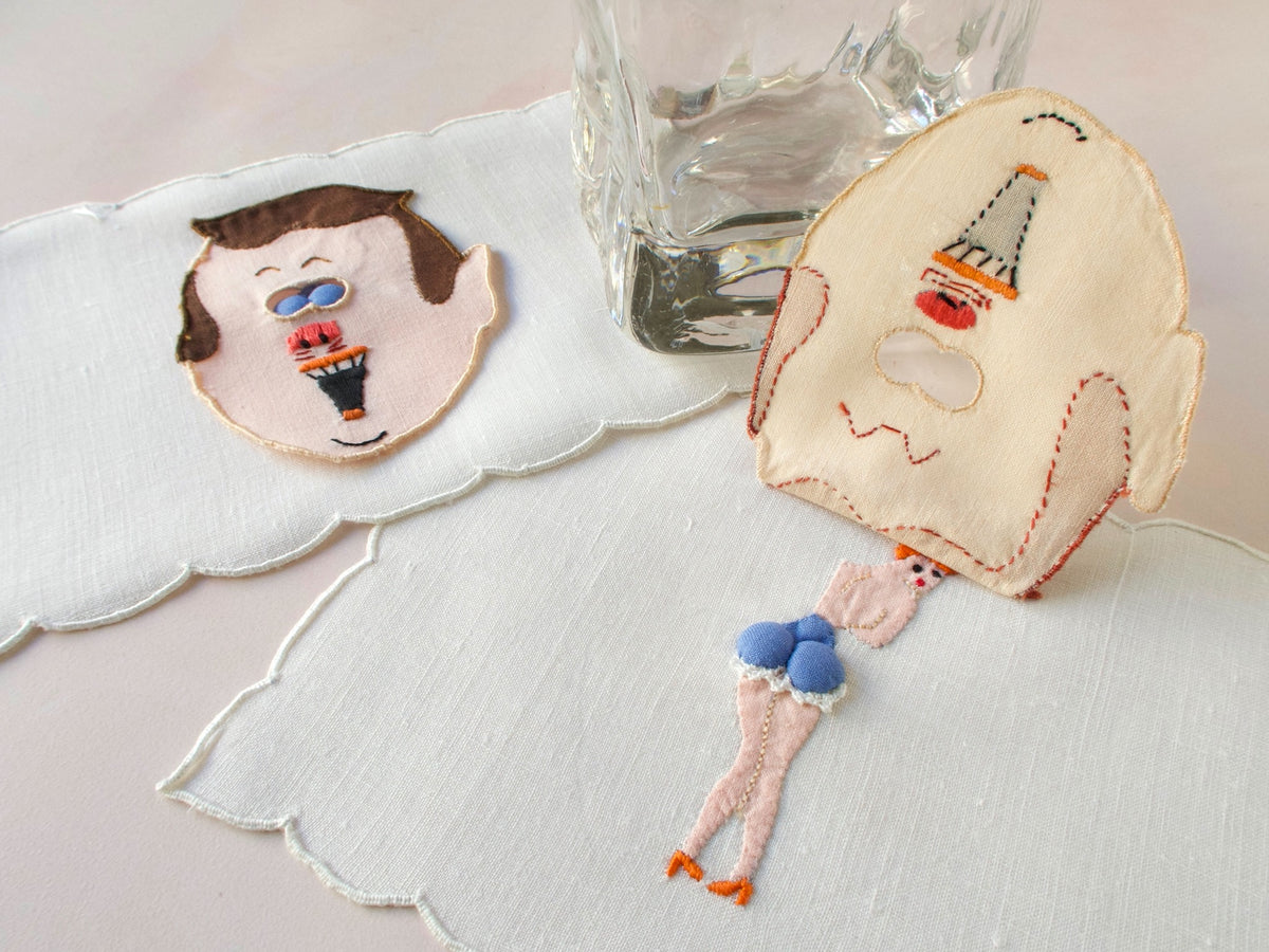 Vintage Madeira peek-a-boo cocktail napkins featuring embroidered men’s faces with blue padded ‘eyes’ that lift to reveal playful pin-up figures underneath. 