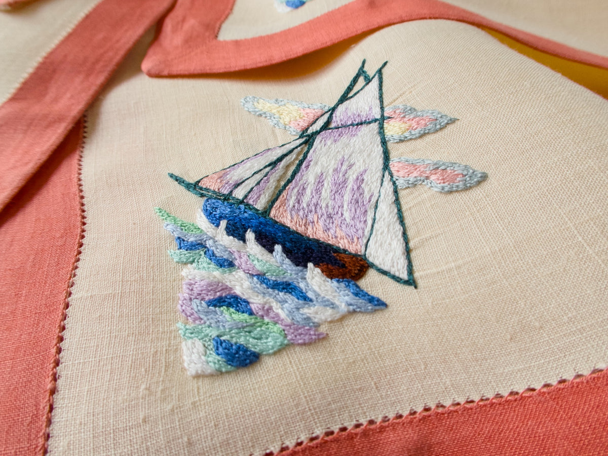 Close view of hand embroidered sailboat on vintage D. Porthault linen, multicolor waves and shaded sails in cotton floss.