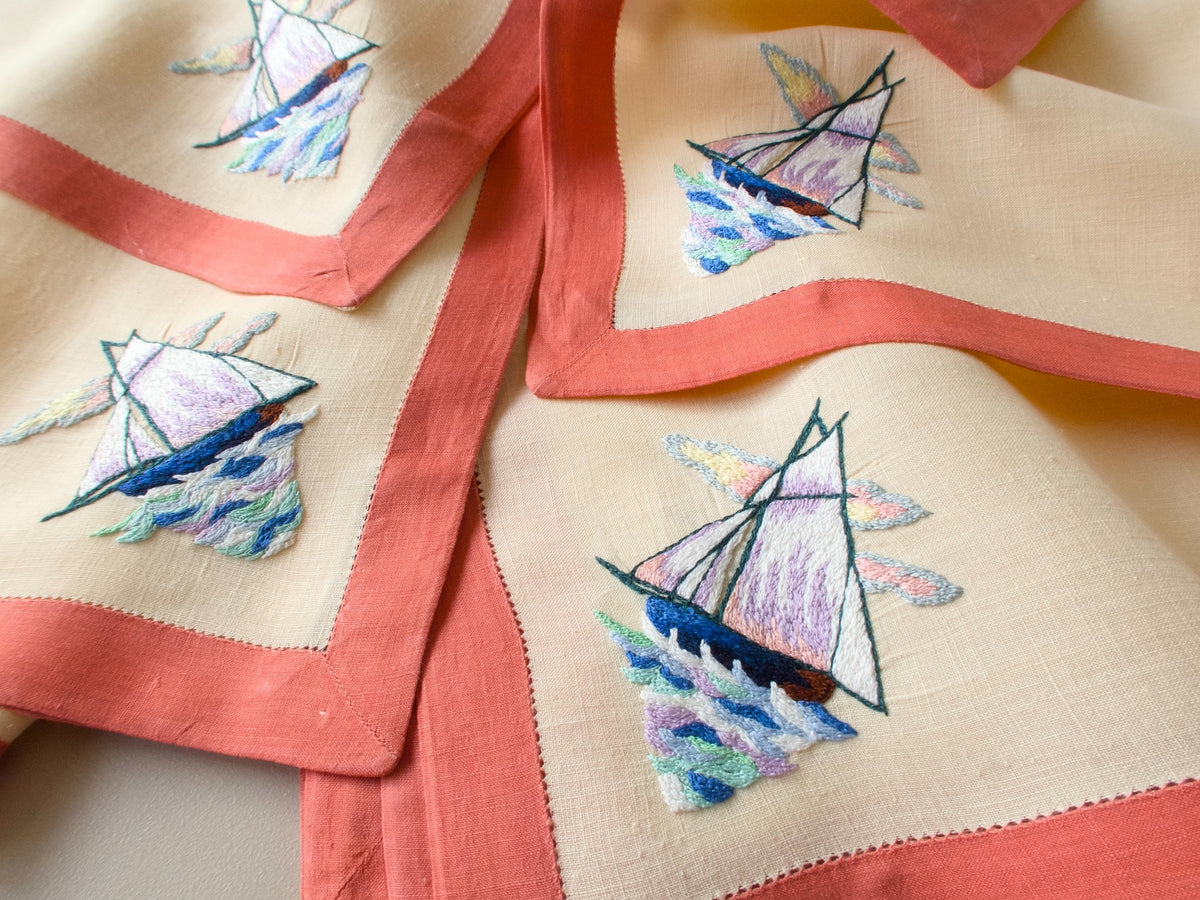Vintage D. Porthault oversized linen table napkins, set of 12, with hand embroidered sailboats and coral border, fanned to show a few from the set.