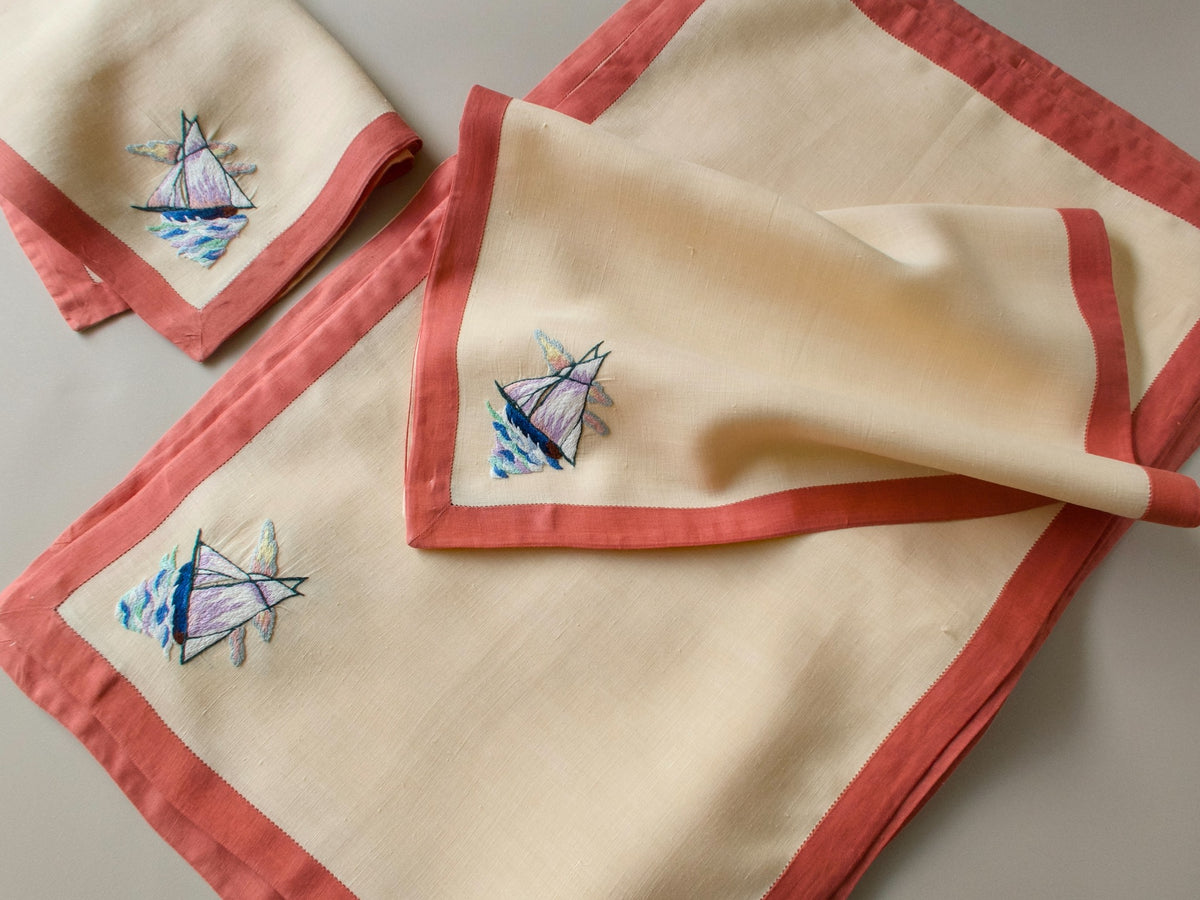 Vintage D. Porthault linen table napkins folded and stacked, showing coral hemstitch border detail.