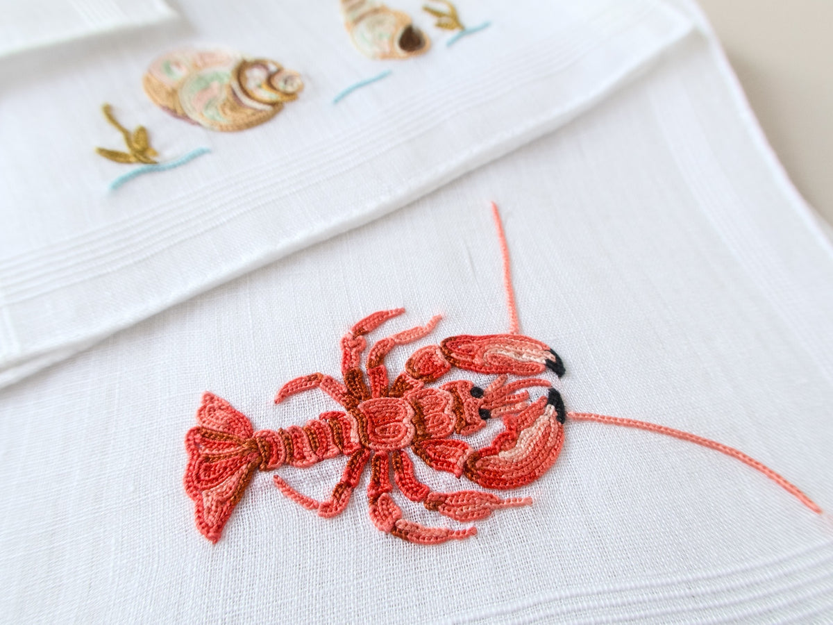 Close view of hand embroidered lobster in Point de Beauvais on vintage French linen cocktail napkin, red and orange detail.