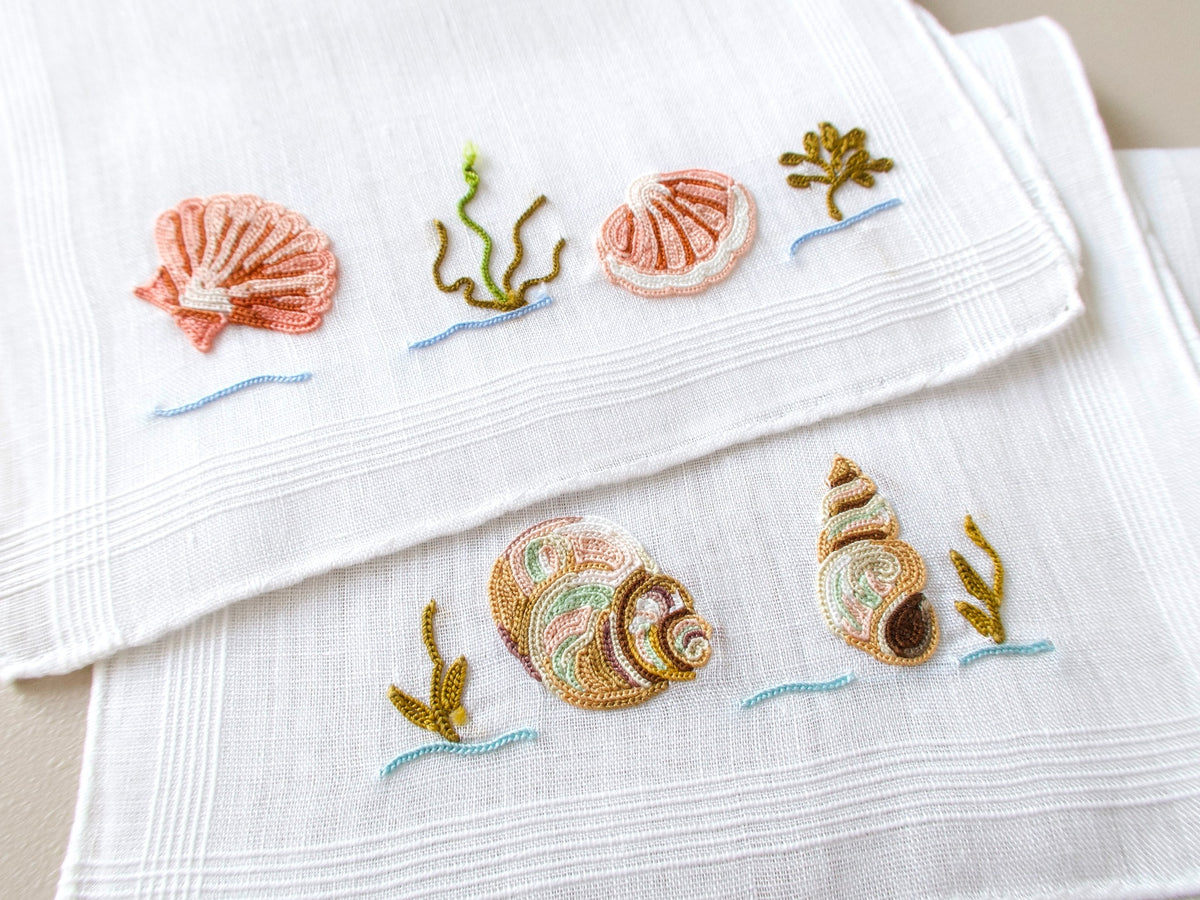 Vintage French Beauvais cocktail napkins fanned and stacked, showing embroidered sea creature motifs on fine white linen.