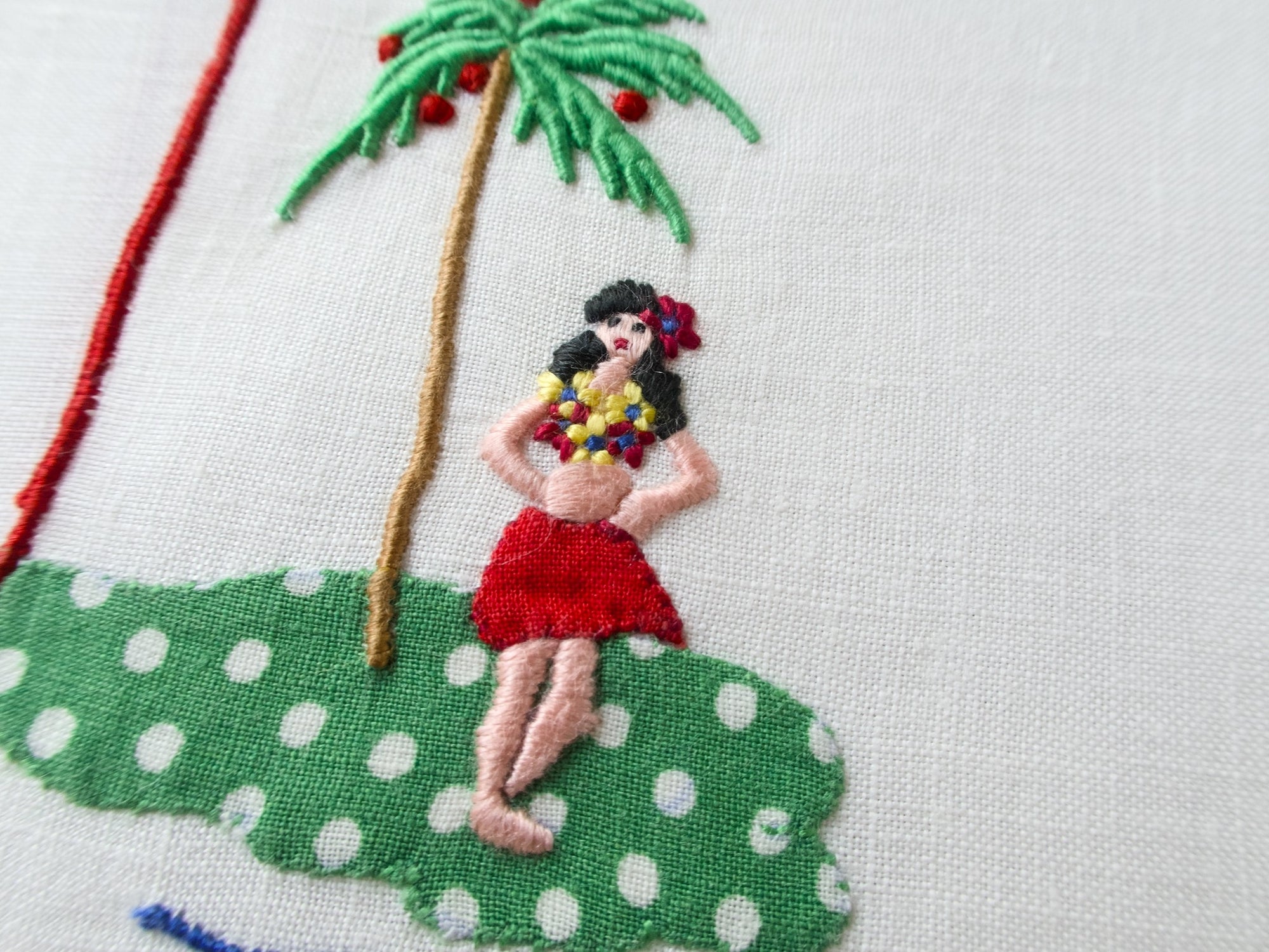 Woman in red skirt and lei standing beneath a palm tree on a hand-embroidered Madeira napkin.