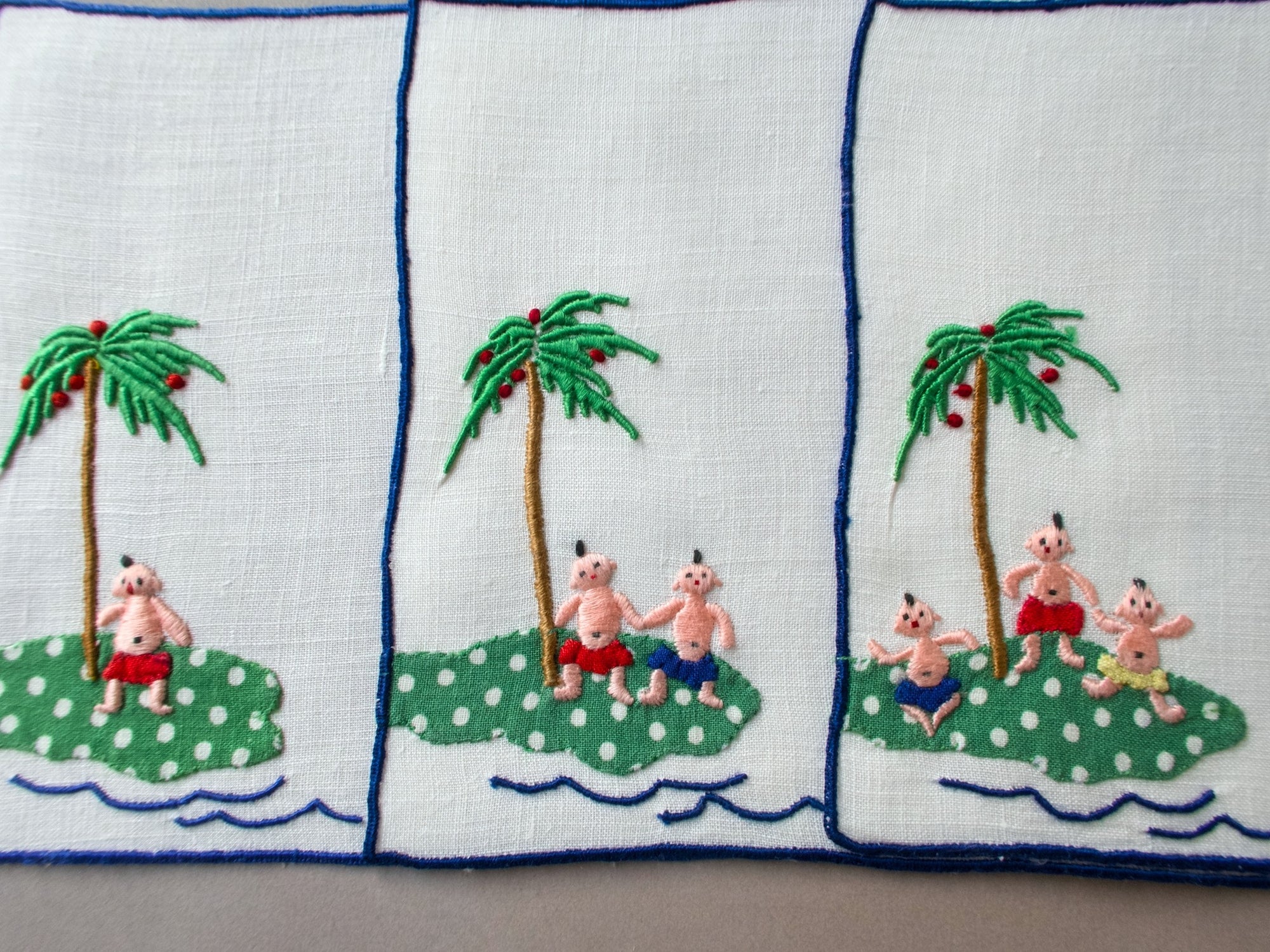 Vintage Madeira cocktail napkins showing playful embroidered scenes of babies on a tropical island beneath palm trees.