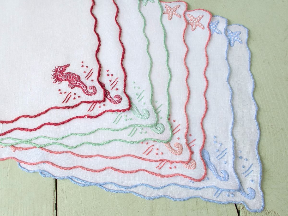 Eight vintage Madeira seahorse cocktail napkins stacked and fanned, showing full color range — pink, blue, green, red, yellow.