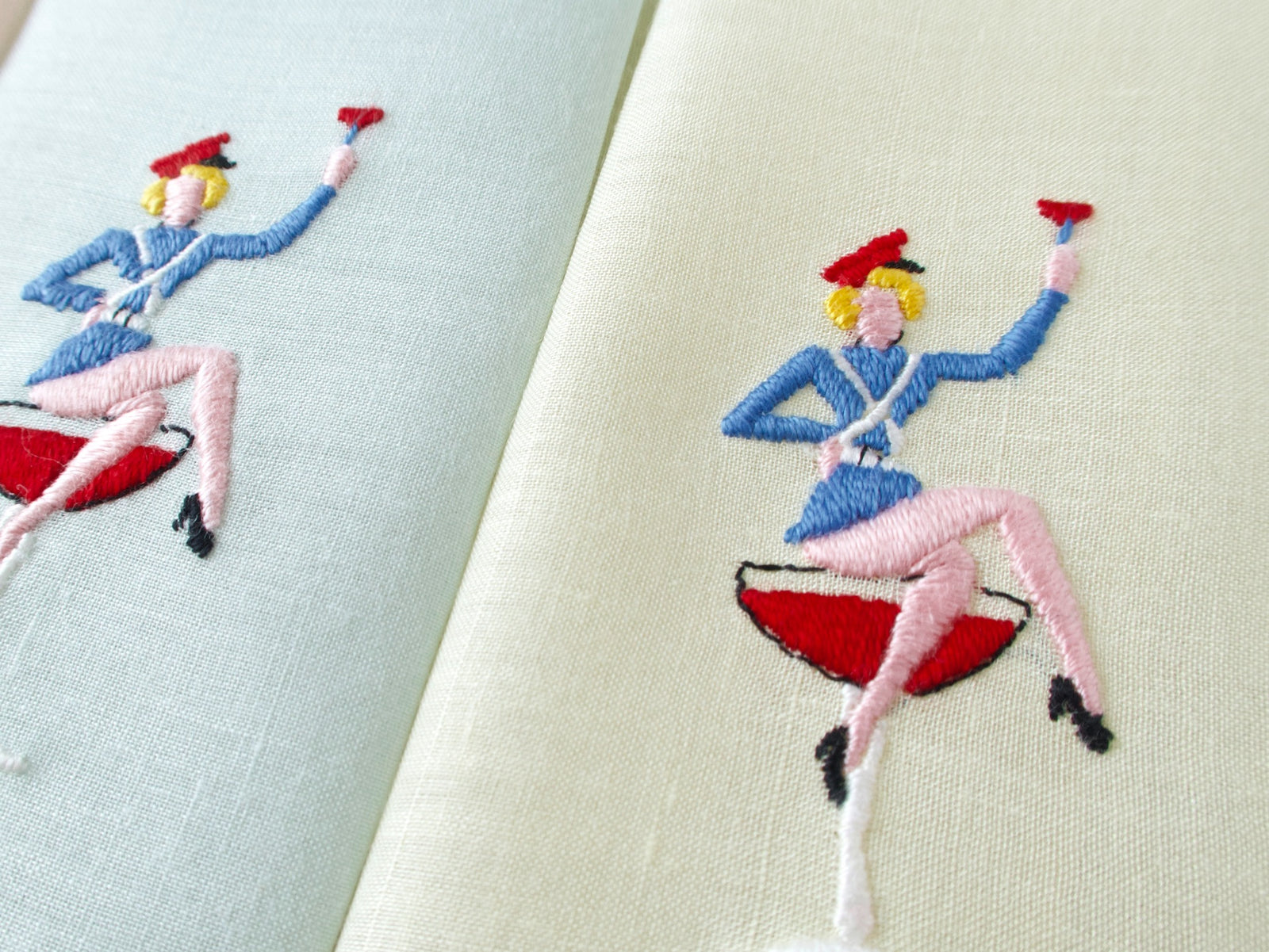 Close view of hand embroidered figure sitting atop a cocktail on vintage Italian semi-sheer linen cocktail napkin, full color detail.​​​​​​​​​​​​​​​​