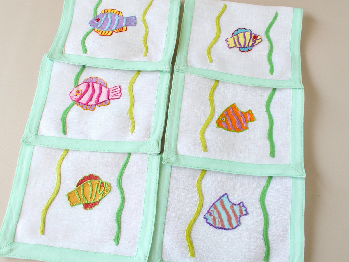 Vintage Léron tropical fish cocktail napkins fanned and stacked, showing colorful fish appliqué and celadon border.