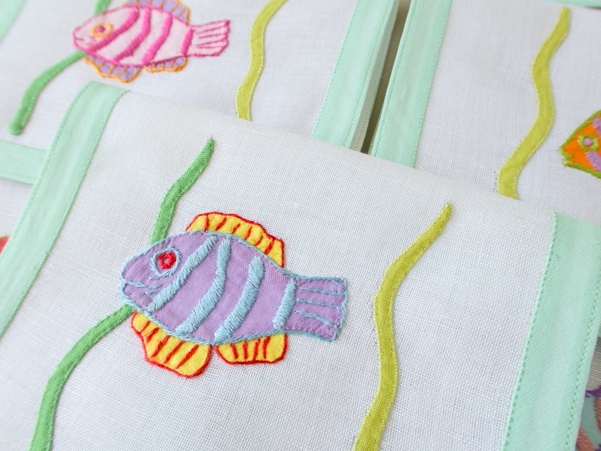 Detail of hand appliquéd tropical fish in orange and green on vintage Léron semi-sheer linen cocktail napkin.