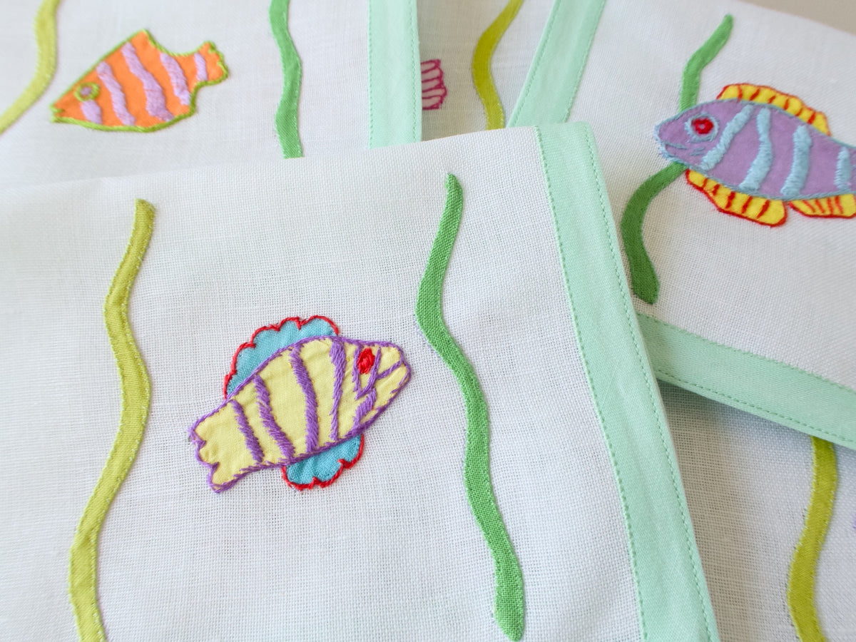 Detail of hand appliquéd tropical fish in pink and purple on vintage Léron semi-sheer linen cocktail napkin.​​​​​​​​​​​​​​​​