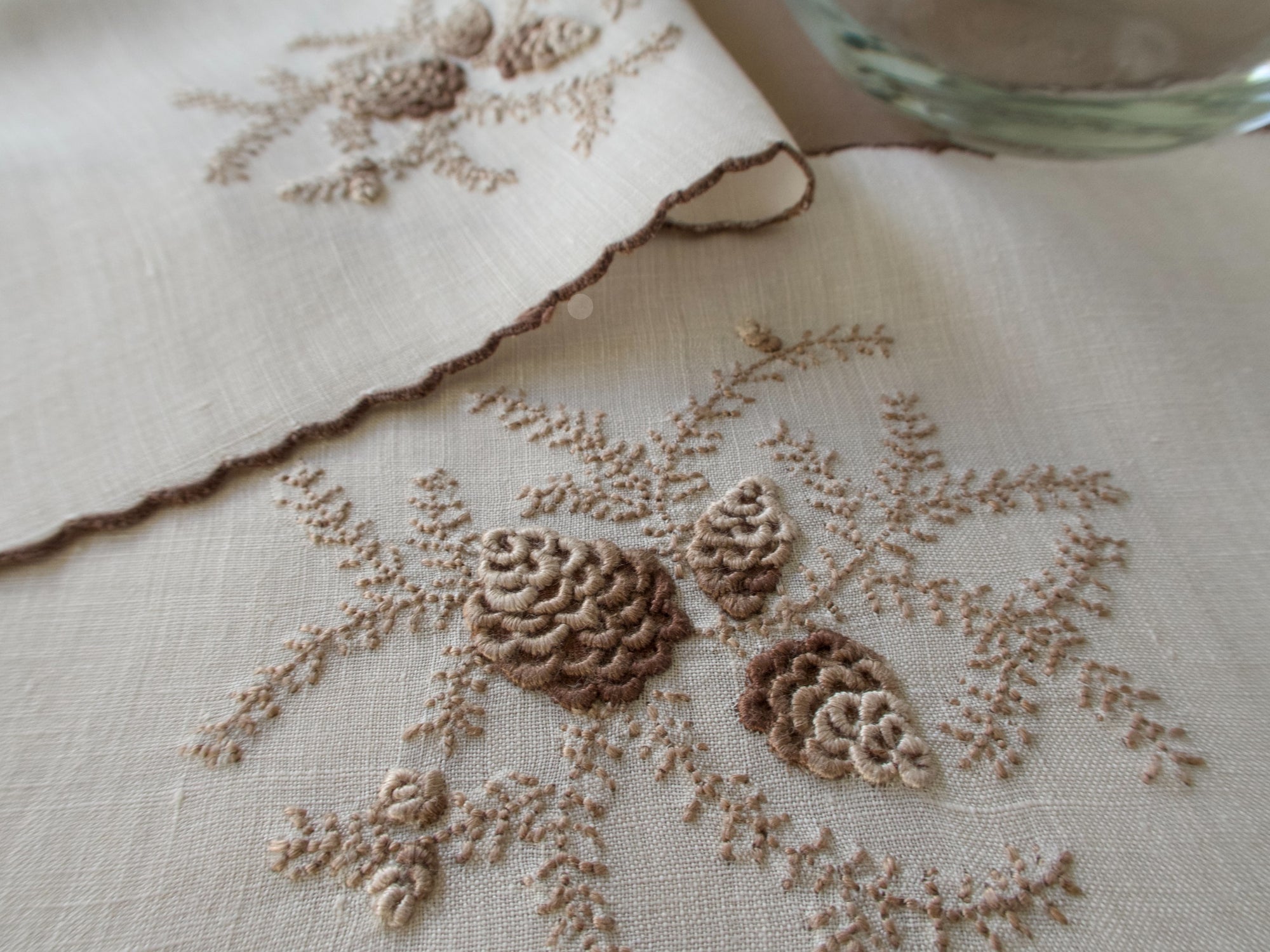 Close-up of embroidered pinecone motif on a vintage Marghab cocktail napkin in the “Pine Cones” pattern on fine linen, hand embroidered in Madeira with raised pinecone motifs and a scalloped edge.