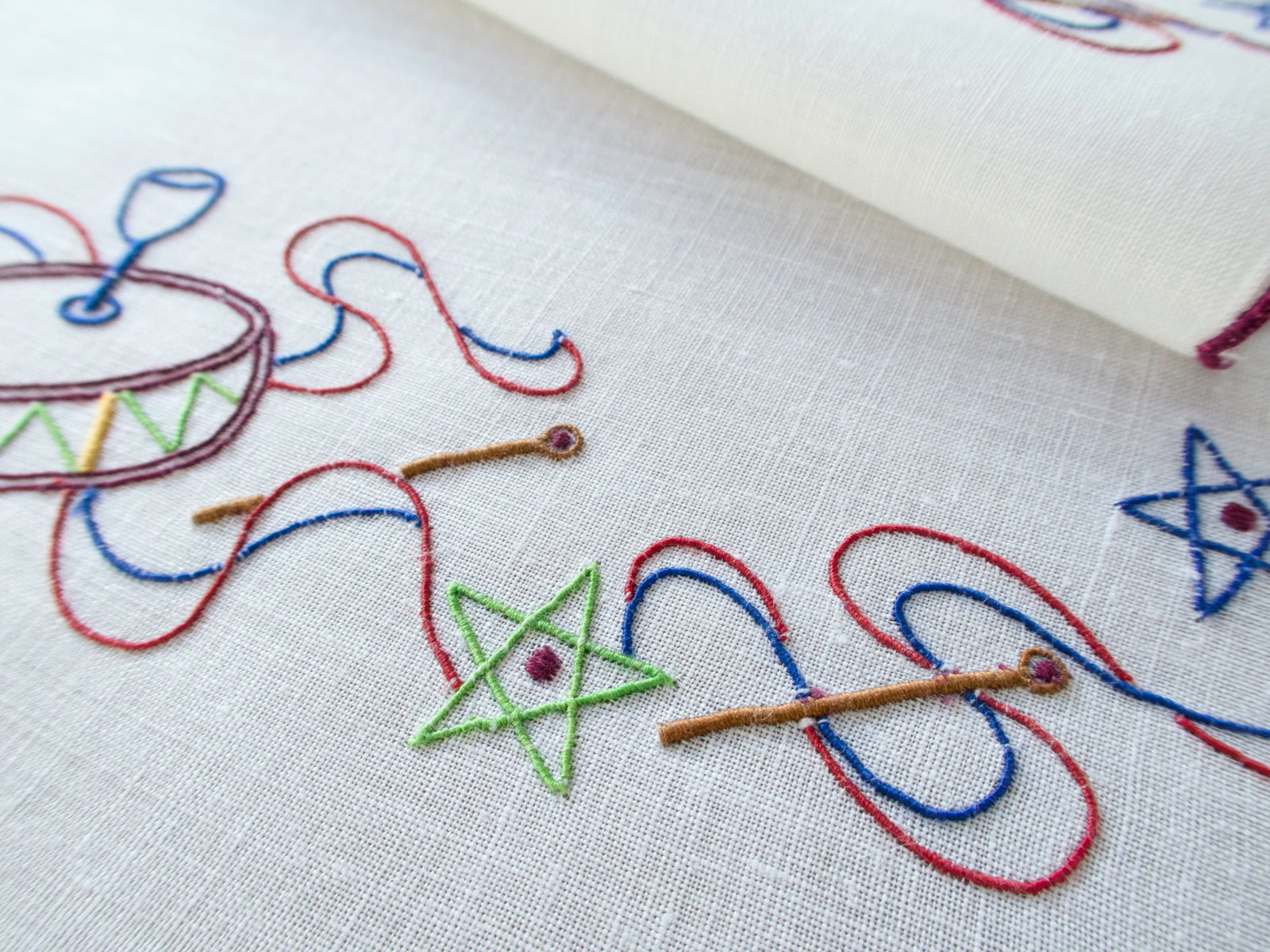 Close-up of embroidered drum & star motif on white linen napkin, hand embroidered in Madeira