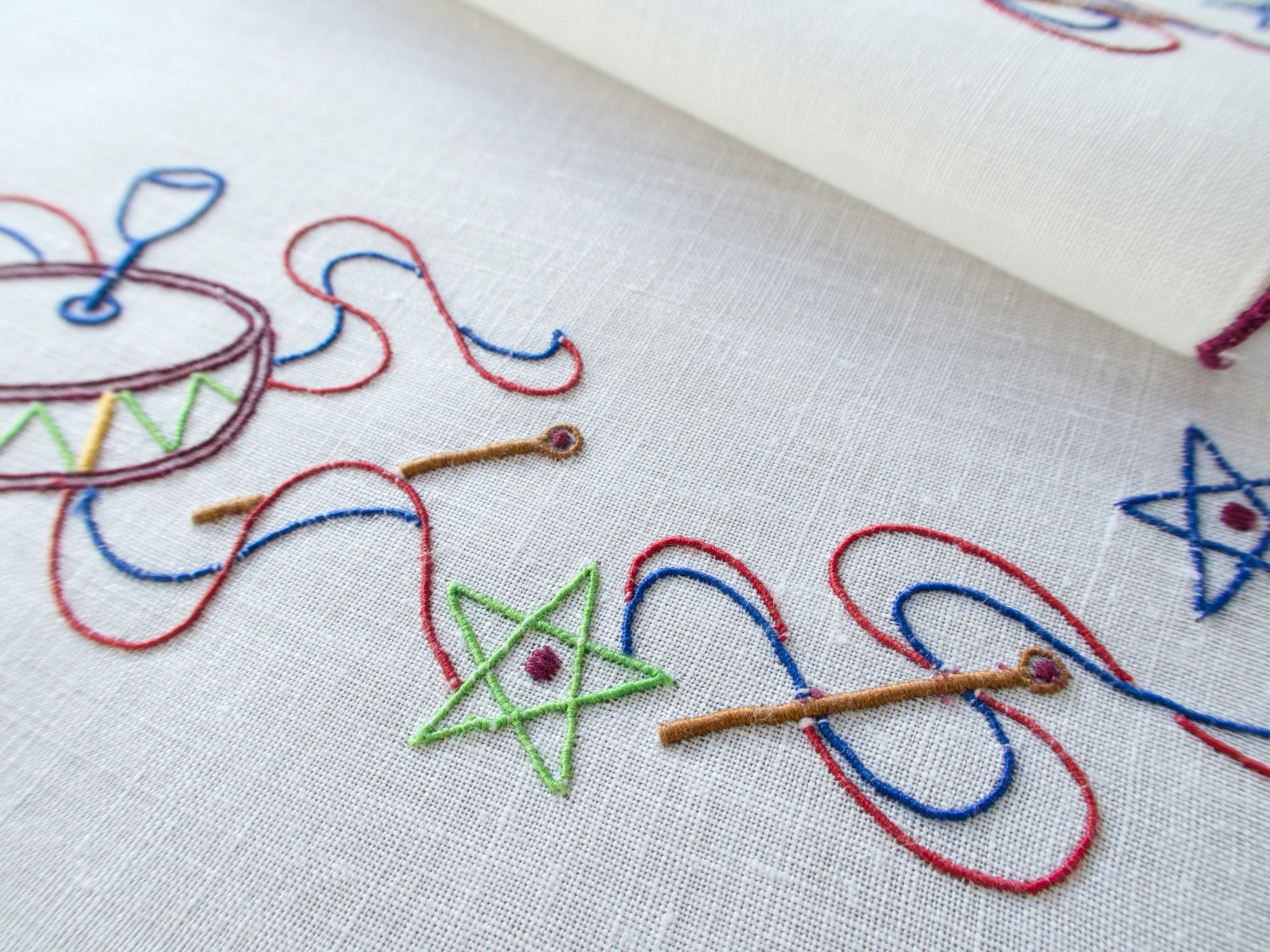 Close-up of embroidered drum & star motif on white linen napkin, hand embroidered in Madeira