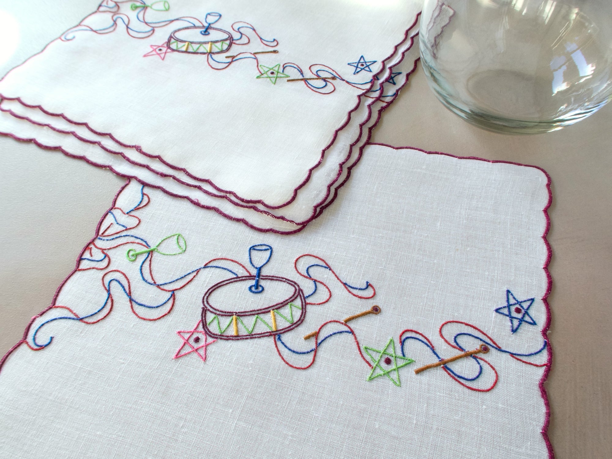 Eembroidered drum & ribbon motif on white linen napkin, hand embroidered in Madeira